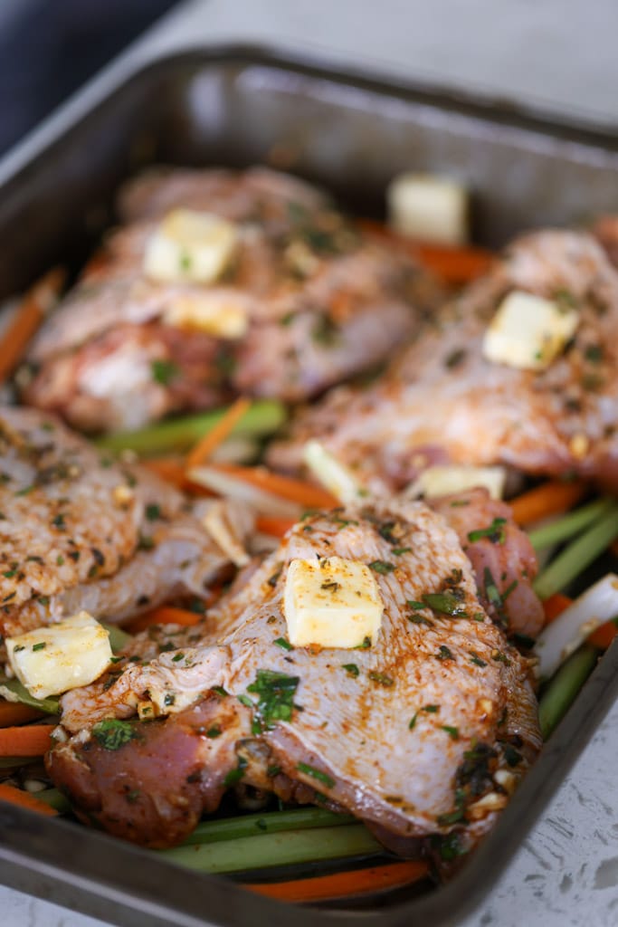 Seasoned turkey thighs in a roasting pan with butter and vegetables before baking.