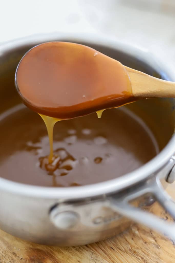 Close-up of glossy rum sauce dripping from a wooden spoon into the saucepan.