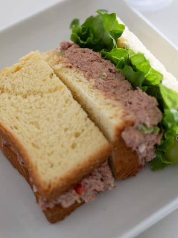 Half of a corned beef sandwich with lettuce on a plate beside green grapes.