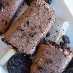 Chocolate cookies and cream pudding pops on a plate with crushed Oreo pieces and wooden sticks.