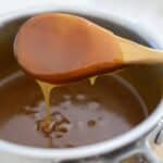 Close-up of glossy rum sauce dripping from a wooden spoon into the saucepan.