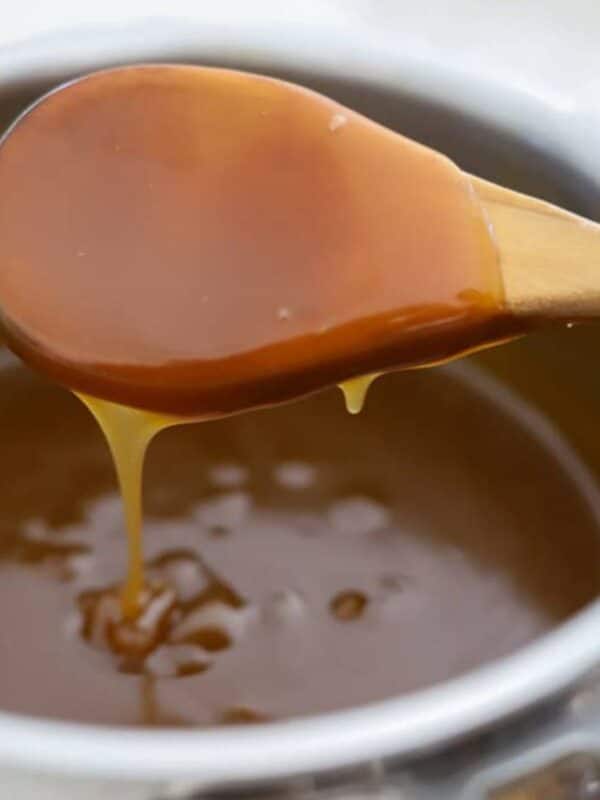 Close-up of glossy rum sauce dripping from a wooden spoon into the saucepan.