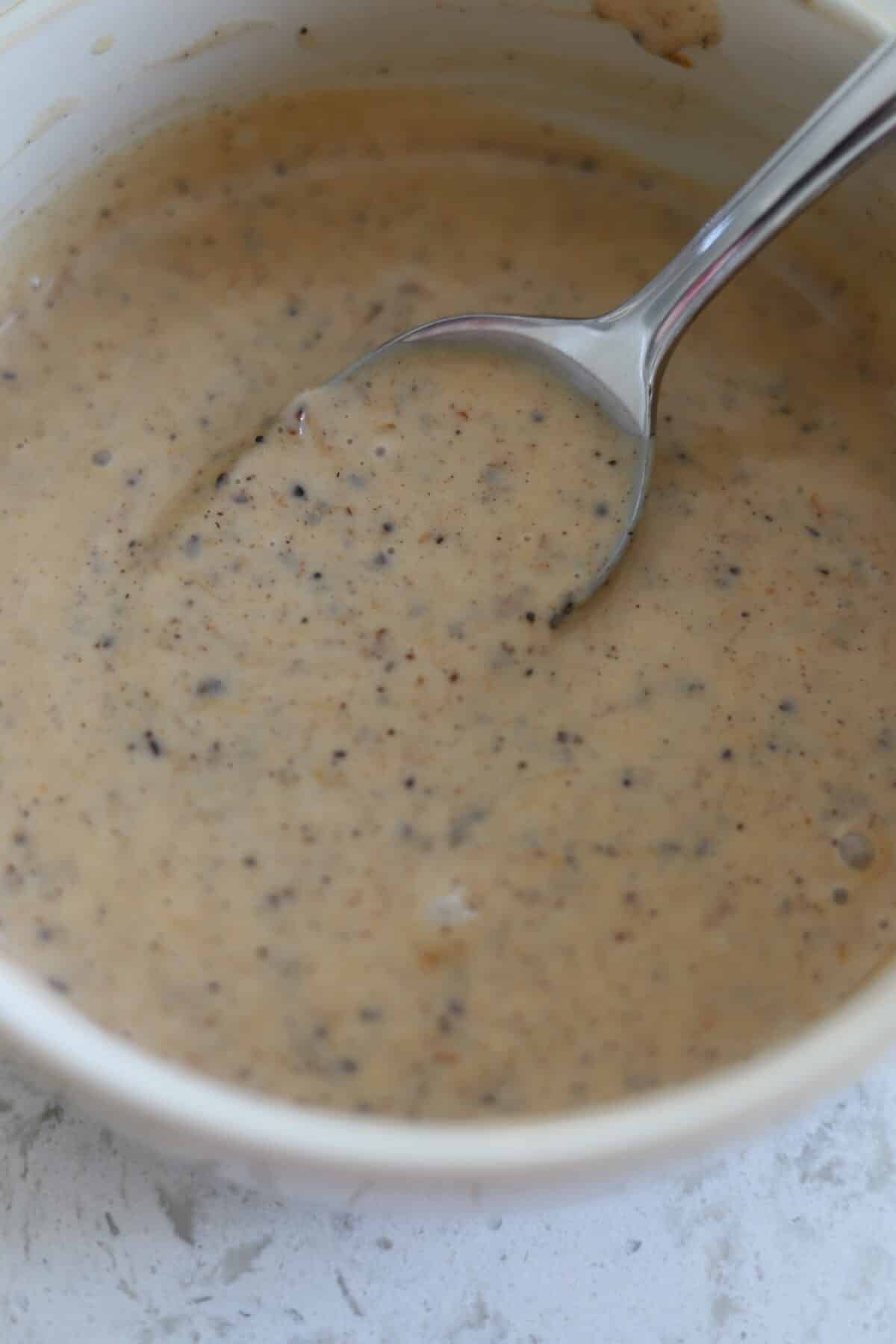 Spoon lifting creamy jerk sauce from a small bowl.