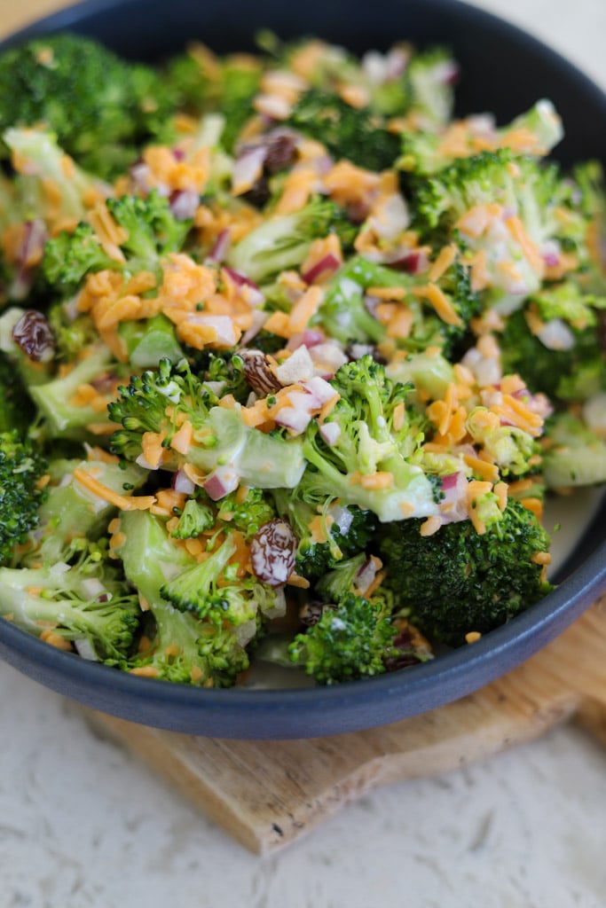Bowl of broccoli salad with cheddar cheese, red onion, and raisins mixed in a creamy dressing.