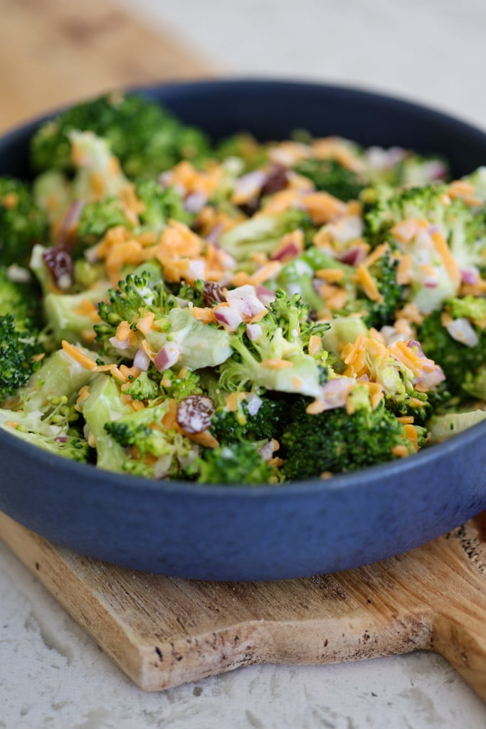 Another angle of broccoli salad in a blue bowl showing broccoli, cheese, onion, and raisins.