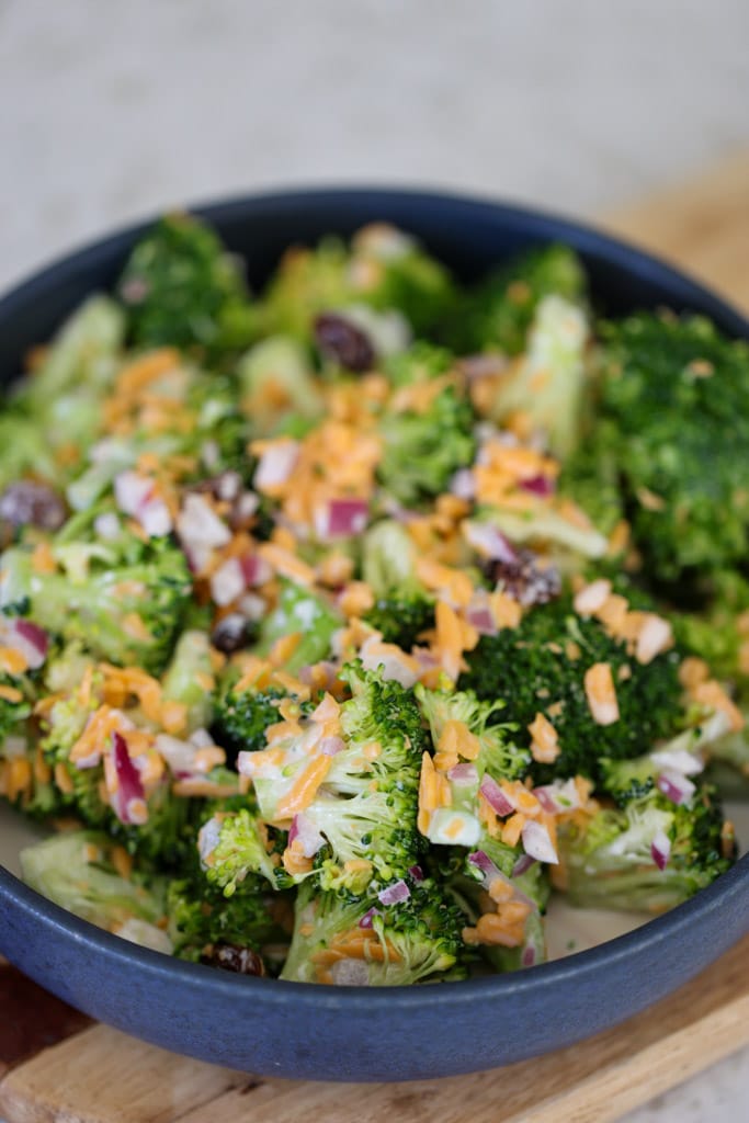 Close-up of broccoli salad highlighting the creamy dressing coating broccoli, cheese, onion, and raisins.