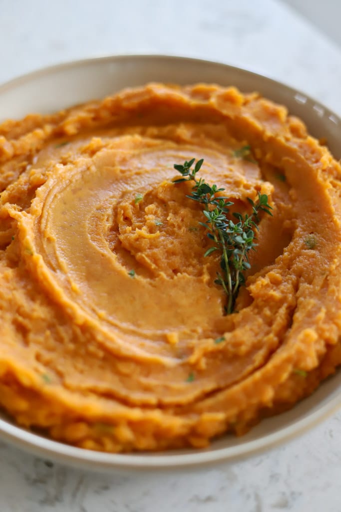 Creamy sweet potato mash in a white bowl, garnished with fresh thyme.