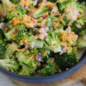 Bowl of broccoli salad with cheddar cheese, red onion, and raisins mixed in a creamy dressing.