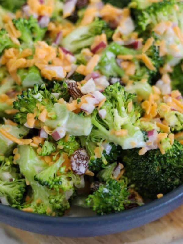 Bowl of broccoli salad with cheddar cheese, red onion, and raisins mixed in a creamy dressing.