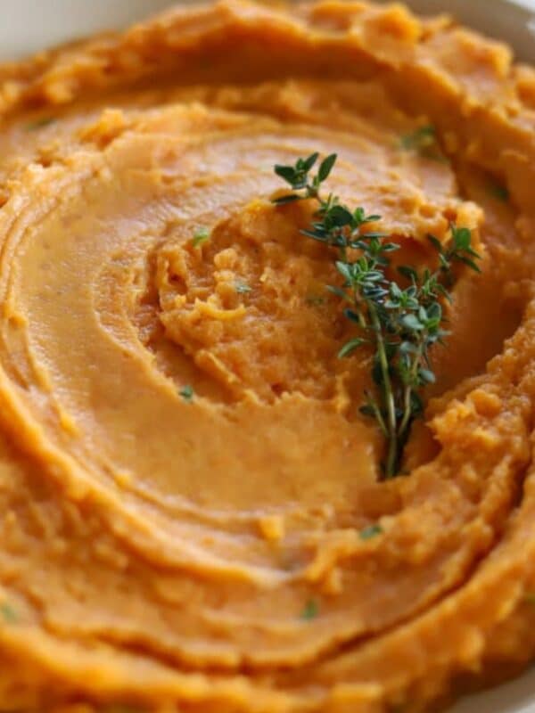 Overhead view of smooth sweet potato mash in a white bowl with thyme garnish.