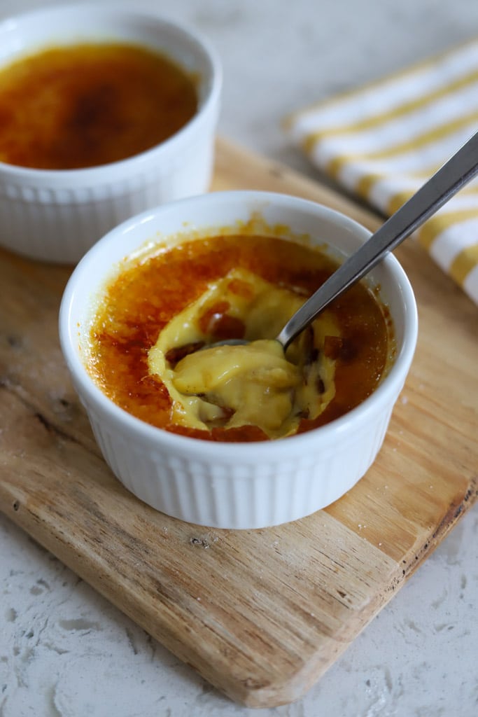 Spoon breaking through the caramelized sugar crust to reveal the silky eggnog custard inside.