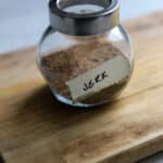 Homemade Jamaican jerk seasoning stored in a glass spice jar labeled jerk on a wooden cutting board