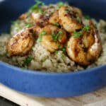 Side view of shrimp risotto in a blue bowl, showing creamy rice topped with seasoned shrimp and herbs.