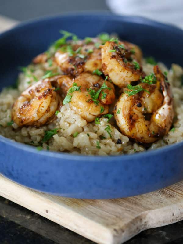 Side view of shrimp risotto in a blue bowl, showing creamy rice topped with seasoned shrimp and herbs.
