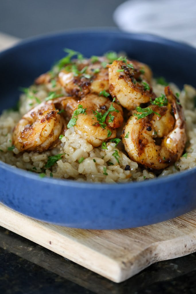 Side view of shrimp risotto in a blue bowl, showing creamy rice topped with seasoned shrimp and herbs.