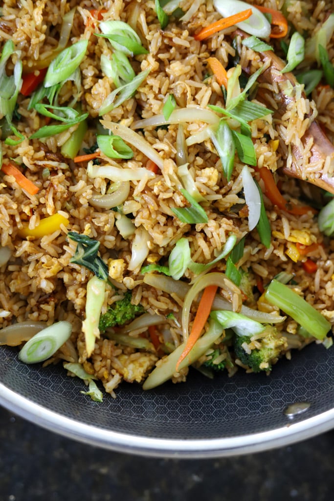 Fried rice mixed with vegetables and garnished with sliced scallions in a wok.