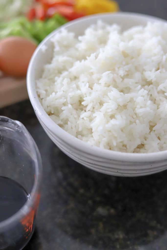 A bowl of freshly cooked white rice with a measuring cup beside it.