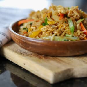 Fried rice mixed with vegetables and garnished with sliced scallions in a wok.