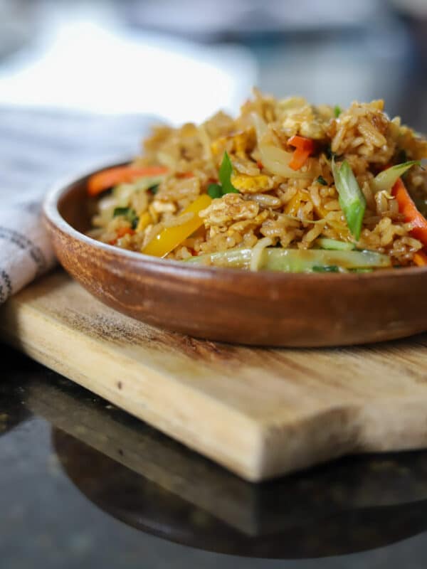 Fried rice mixed with vegetables and garnished with sliced scallions in a wok.
