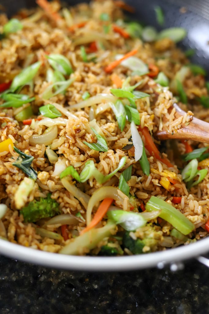 Fried rice mixed with vegetables and garnished with sliced scallions in a wok.