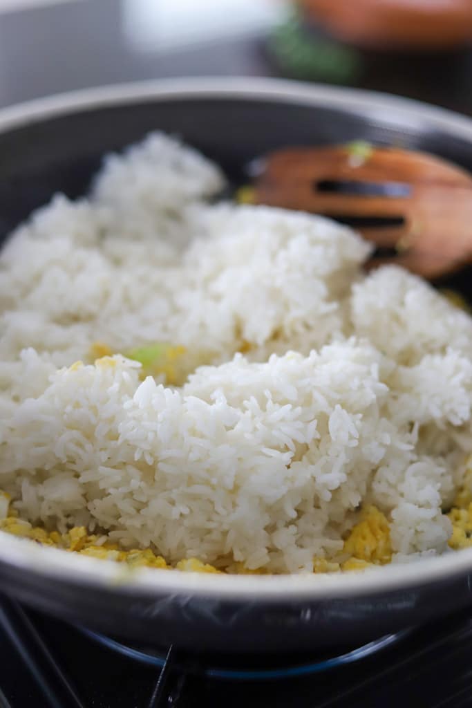 Cooked white rice being stirred in a pan with a wooden spoon.