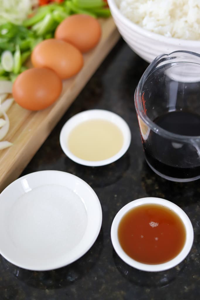 Small bowls of sauce ingredients with eggs and a measuring cup of soy sauce on a countertop.