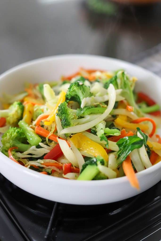 A bowl of mixed stir-fried vegetables including bok choy, carrots, broccoli, and bell peppers.