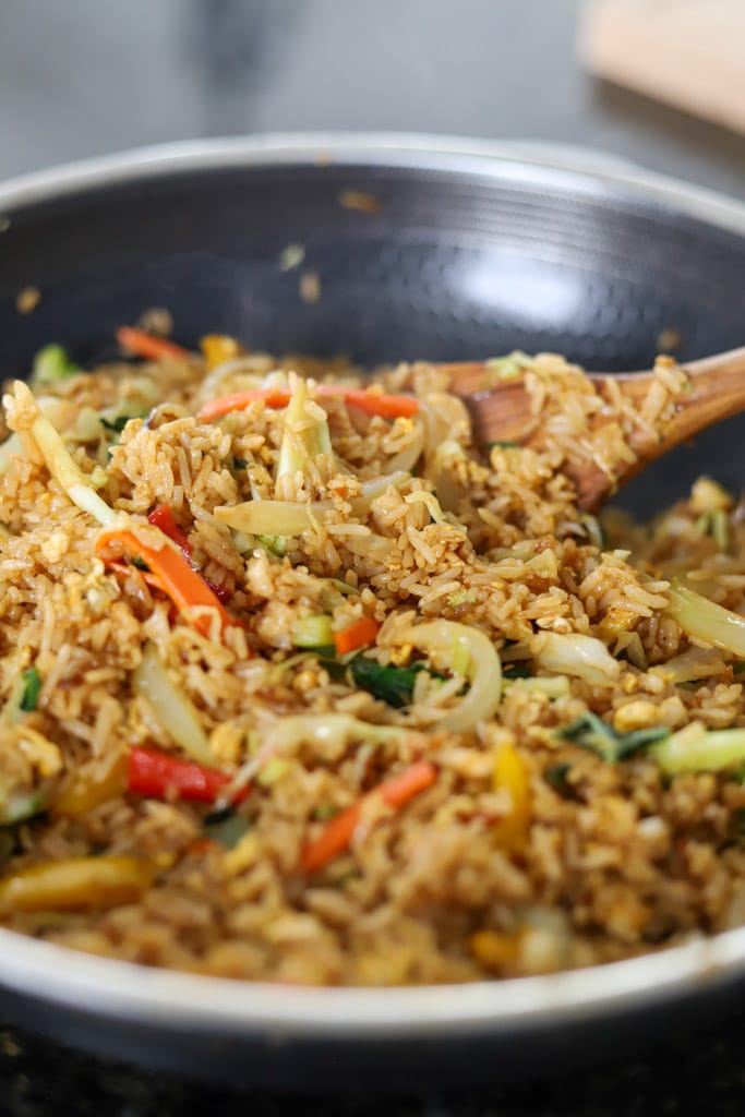 Vegetable fried rice cooking in a wok with visible cabbage, carrots, and peppers.