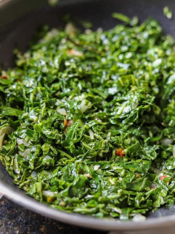 sautéed collard greens with onion and tomato in pan.