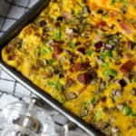 Golden sheet pan omelette sliced into portions with bacon, ham, vegetables, and cheese, ready to serve.
