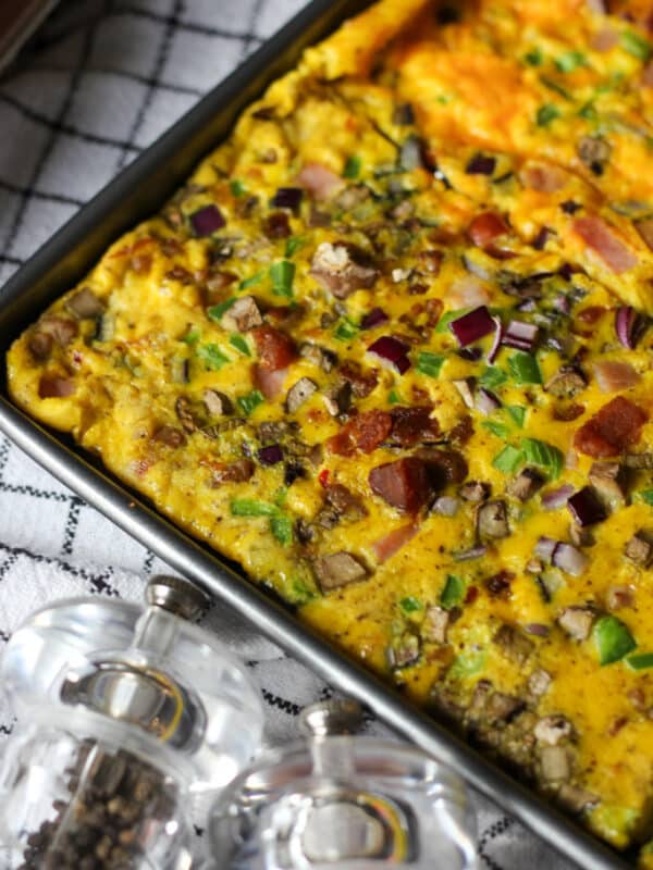 Golden sheet pan omelette sliced into portions with bacon, ham, vegetables, and cheese, ready to serve.